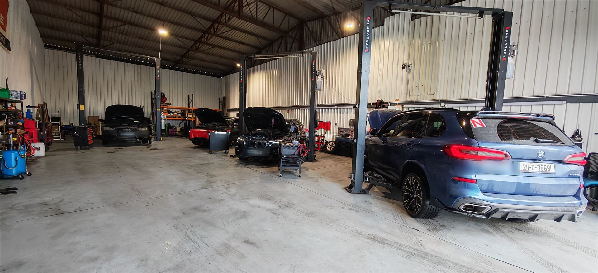 Blue BMW X5 parked in a service bay between two-post lifts with other cars being repaired in the workshop