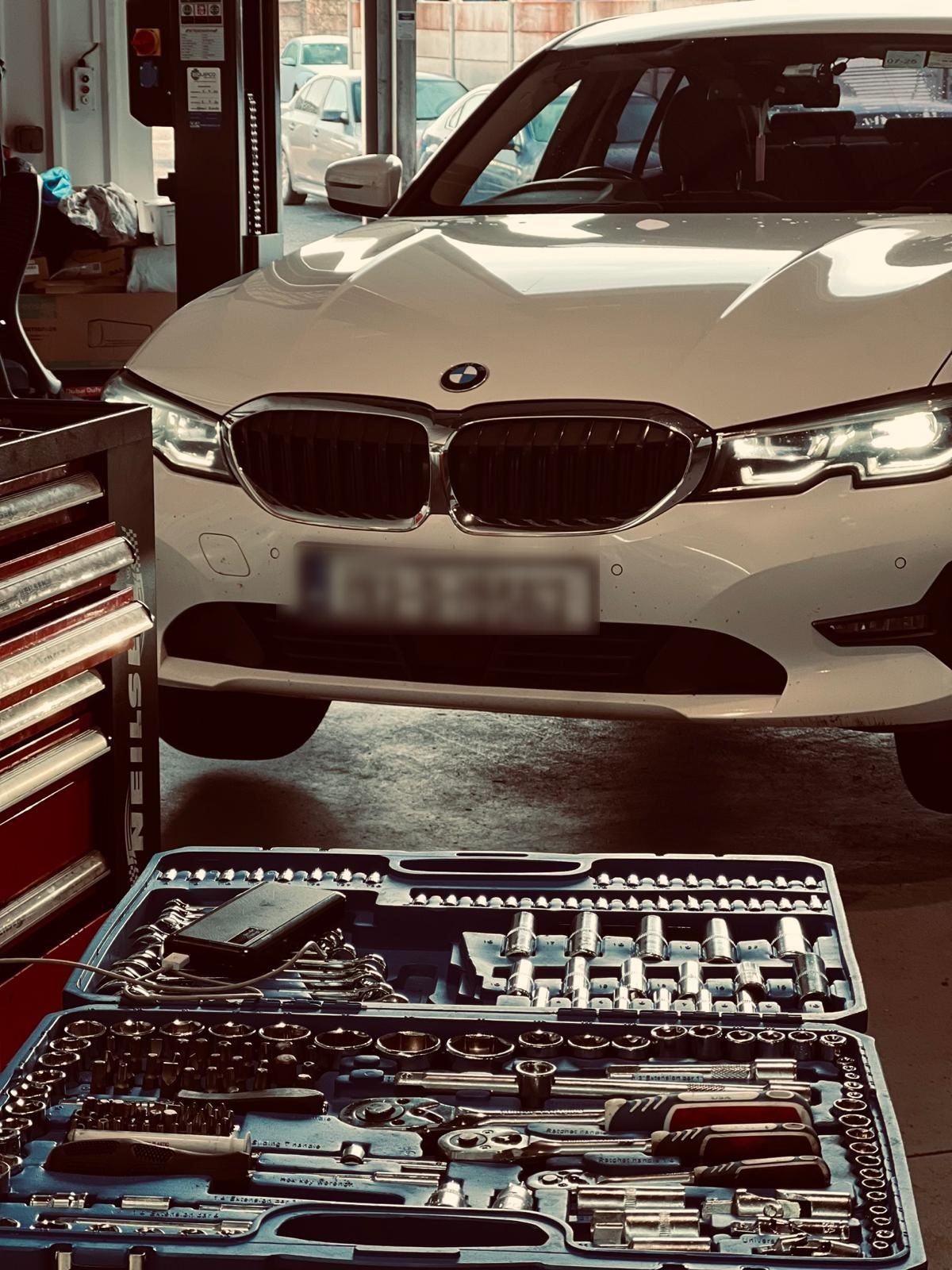 Open socket and wrench tool sets in cases in front of a white BMW inside an auto repair garage