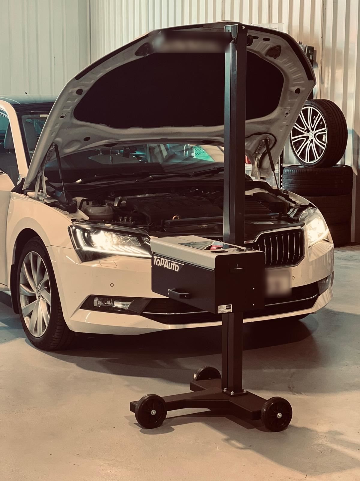 Headlight alignment testing equipment set up in front of a car with its hood open in a garage